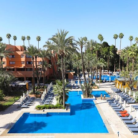 Hotel Kenzi Rose Garden Marrakesh Exterior foto The photo shows a resort-style area with several swimming pools surrounded by palm trees. The pools are clear blue and are lined with numerous lounge chairs for relaxation. There is a vibrant atmosphere, highlighted by lush greenery and a sunny sky. 